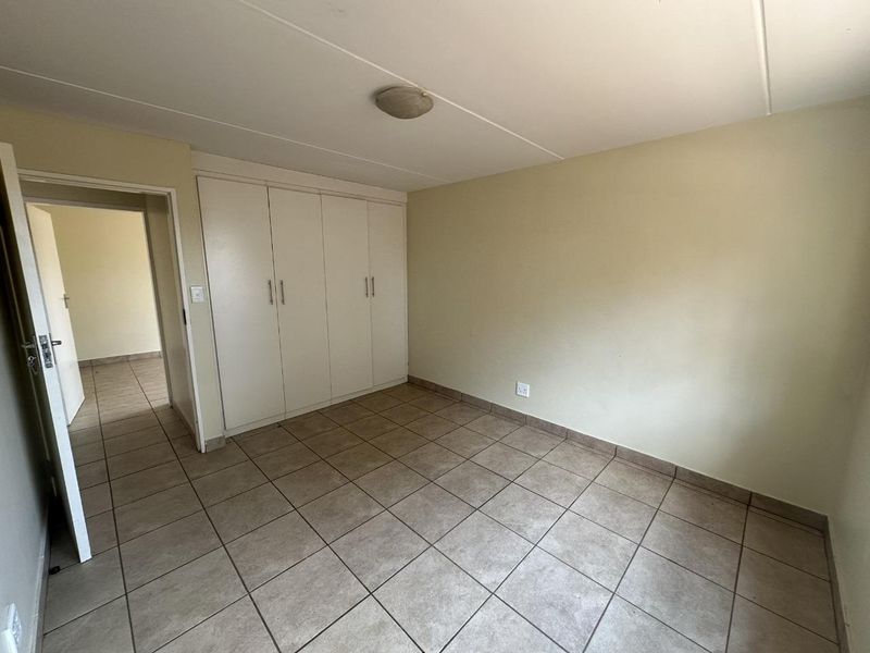 A clean, empty bedroom featuring neutral tiled flooring and built-in storage cupboards, offering a blank canvas for personalization.