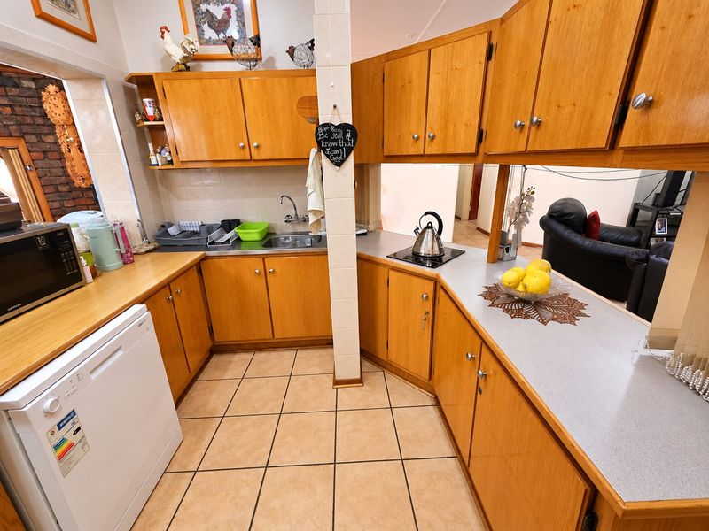 A functional kitchen featuring wood-look laminate cabinetry, tiled flooring, and a built-in hob, offering a practical layout with potential for modern cosmetic updates.