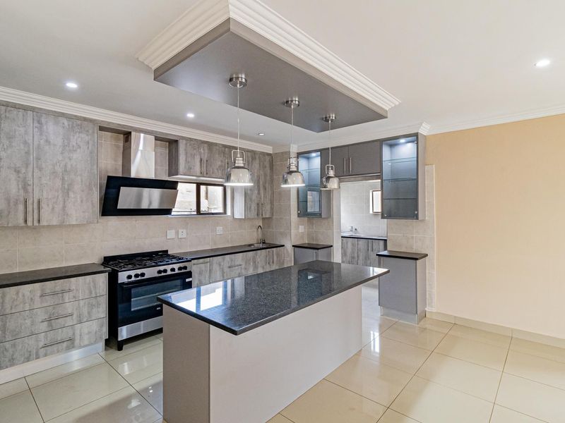 Modern kitchen featuring a central island, granite countertops, gas stove, extractor fan, and ample built-in cabinetry with a seamless transition to the scullery.
