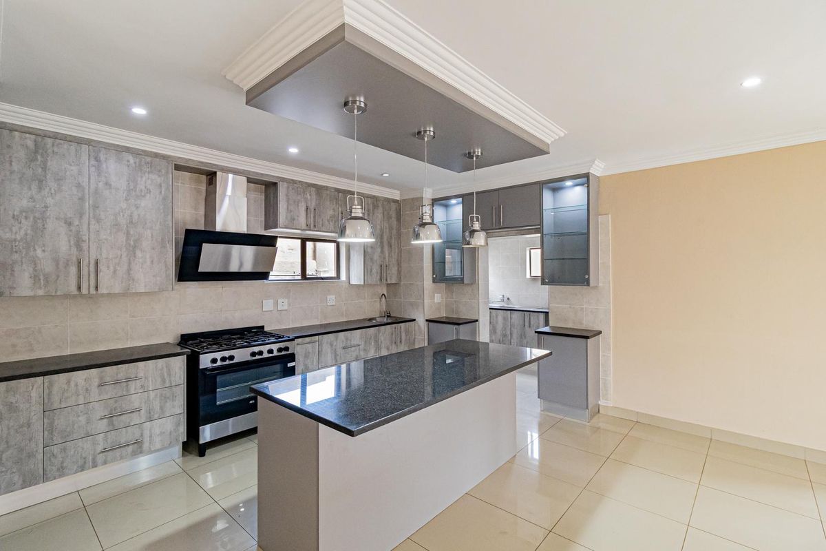Modern kitchen featuring a central island, granite countertops, gas stove, extractor fan, and ample built-in cabinetry with a seamless transition to the scullery.