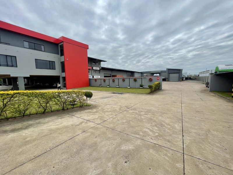 Exterior view of an industrial property featuring a large concrete driveway, warehouse facade, and covered parking area.