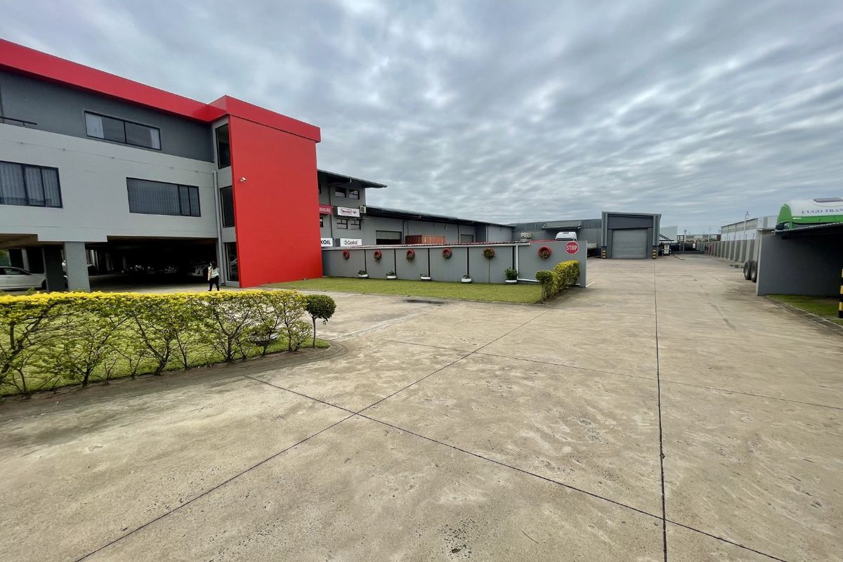 Exterior view of an industrial property featuring a large concrete driveway, warehouse facade, and covered parking area.