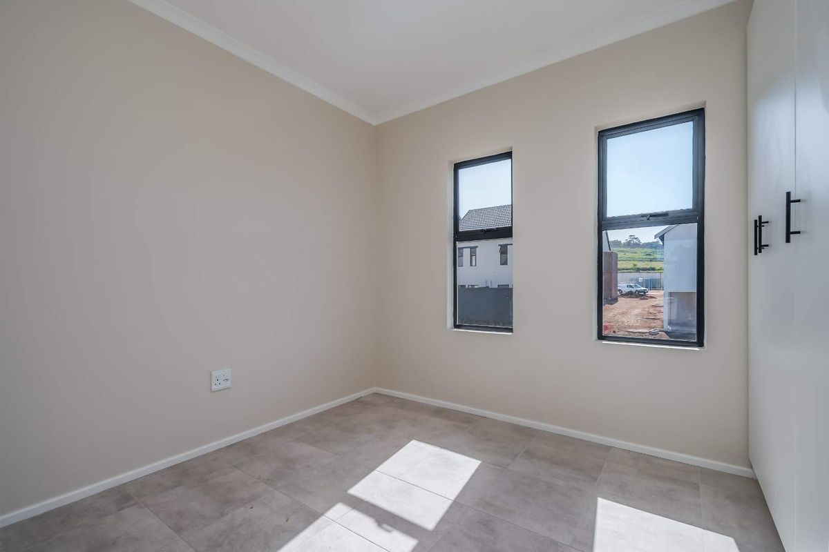 A bright, empty bedroom featuring neutral wall tones, tiled flooring, and built-in cupboards with modern black hardware.