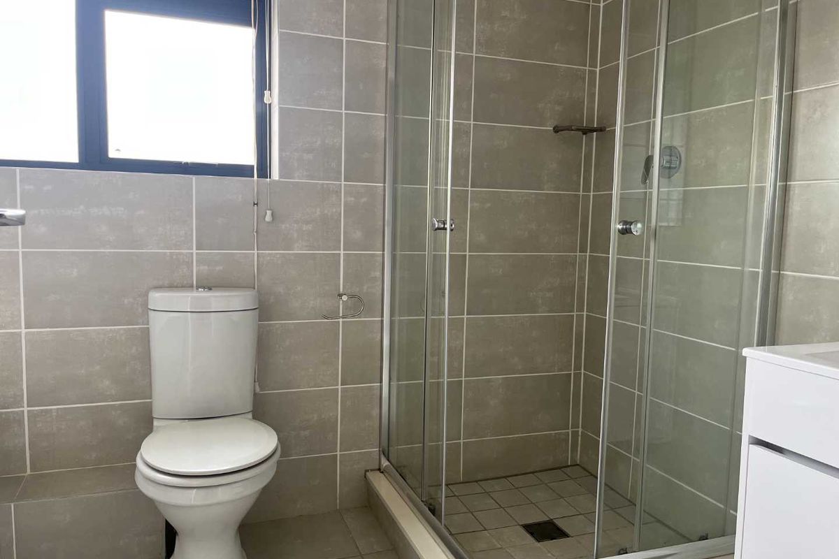 A modern bathroom featuring a glass-enclosed shower, a white toilet, and neutral wall tiling with a window for natural light.