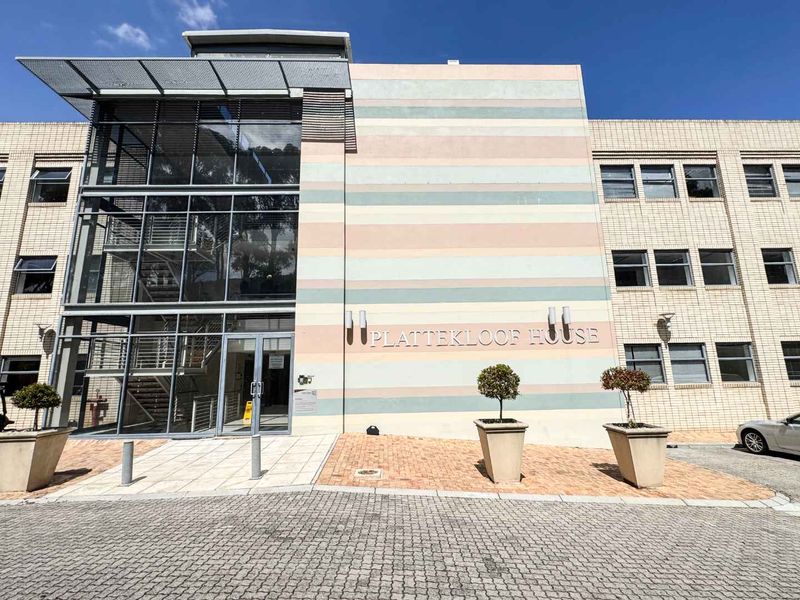 Front exterior view of Plattekloof House, featuring a modern glass facade, steel staircase, and paved entrance area.