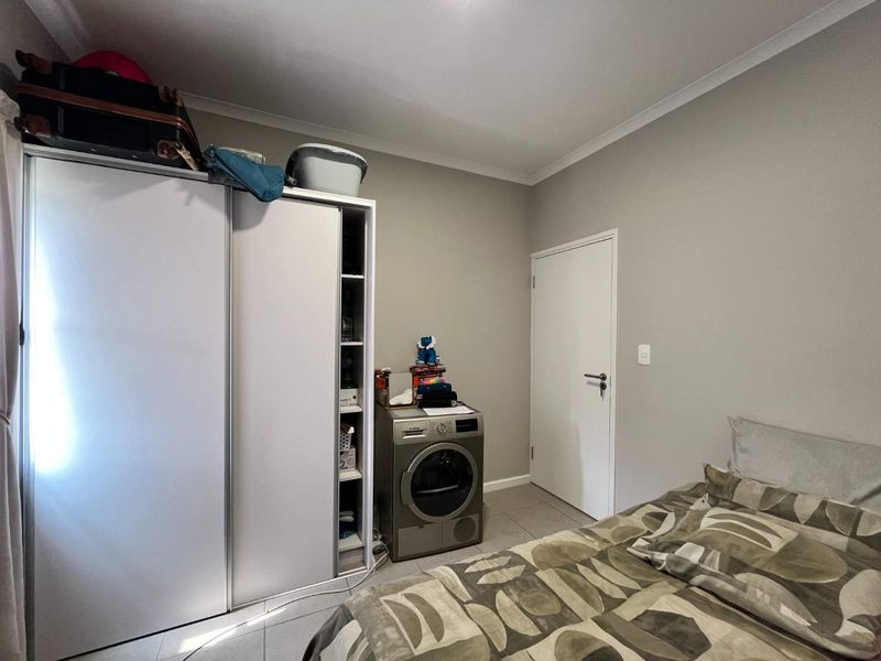 A bedroom featuring tiled flooring, a built-in wardrobe, and neutral wall finishes, currently accommodating a laundry appliance.