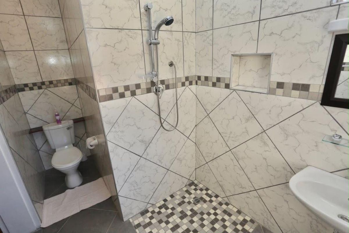 A functional bathroom featuring a walk-in shower with a built-in niche, a standard toilet, and a wall-mounted wash basin with tiled finishes.
