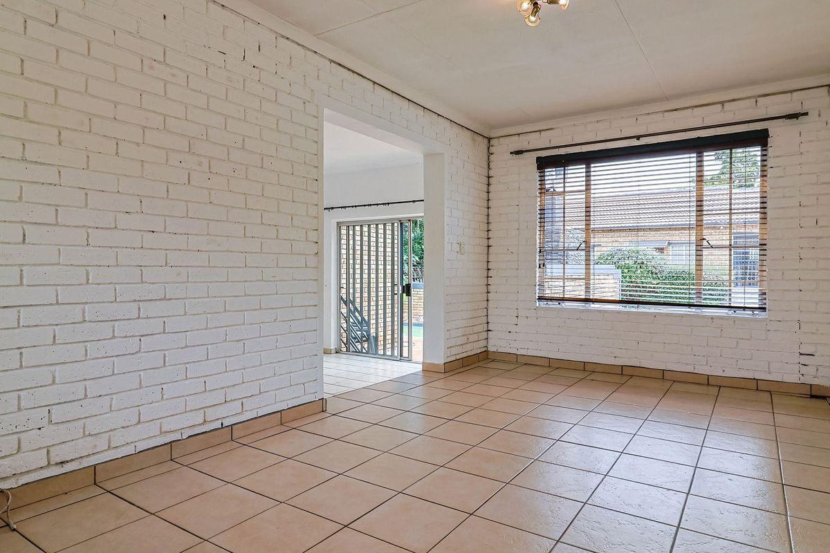 An empty living area featuring white painted brick walls, ceramic floor tiles, and a large window with fitted blinds.