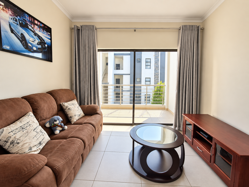 A well-lit living room featuring large sliding glass doors that open onto a private balcony, finished with neutral floor tiles and modern curtain fixtures.