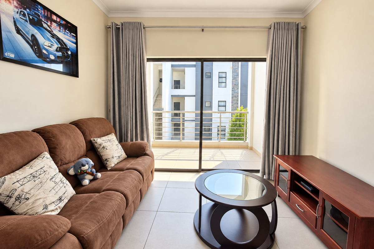 A well-lit living room featuring large sliding glass doors that open onto a private balcony, finished with neutral floor tiles and modern curtain fixtures.