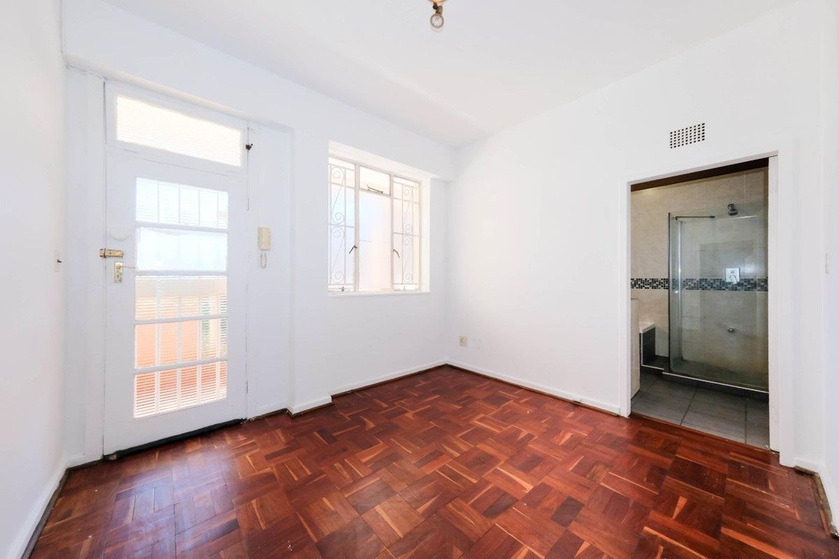 Empty bedroom featuring classic parquet flooring, a security-gated exterior door, and direct access to an en-suite bathroom with a glass shower enclosure.
