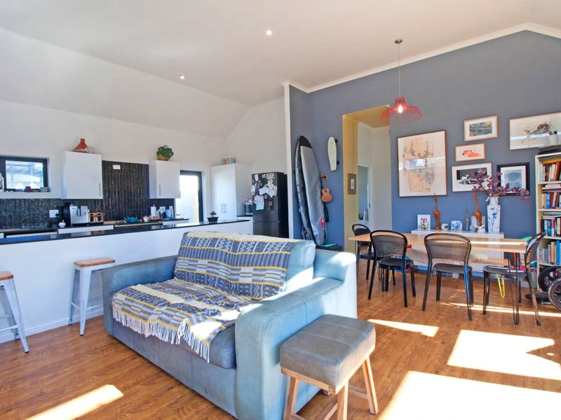 Open-plan living and dining area featuring a modern kitchen with dark tiled backsplash, island, and warm laminate flooring throughout.