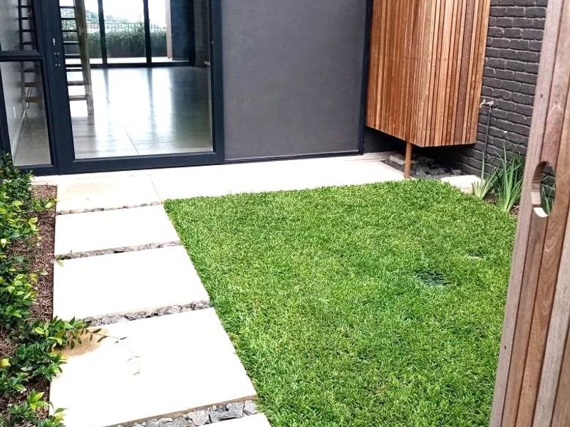 A private rear courtyard featuring a manicured lawn, stone paver path, and a modern timber privacy screen adjacent to the main living area.