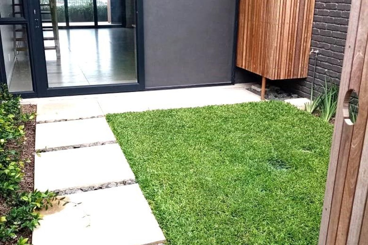 A private rear courtyard featuring a manicured lawn, stone paver path, and a modern timber privacy screen adjacent to the main living area.