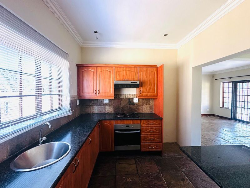 Functional kitchen featuring wooden cabinetry, granite countertops, built-in oven, gas hob, and stone tile flooring, with an open-plan flow to the adjacent living area.