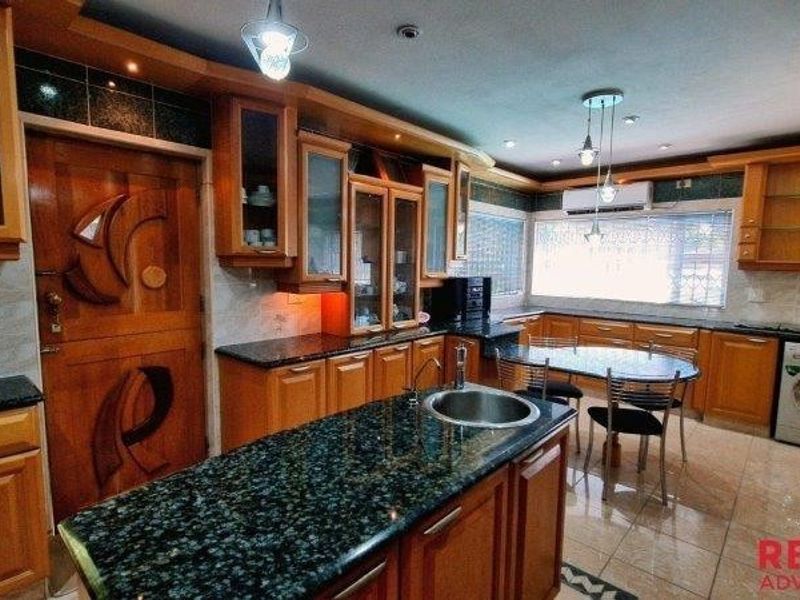 Spacious kitchen featuring extensive wooden cabinetry, granite countertops, a central island with sink, and integrated appliances, offering a functional and traditional layout.