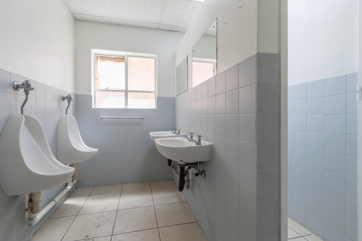 Functional industrial restroom facility featuring wall-mounted urinals, dual ceramic washbasins, and tiled wall finishes.