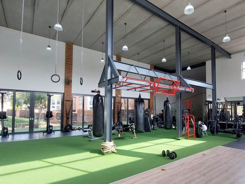 A spacious, modern gym facility featuring high ceilings with exposed steel beams, rubber and turf flooring, and large glass doors providing natural light.