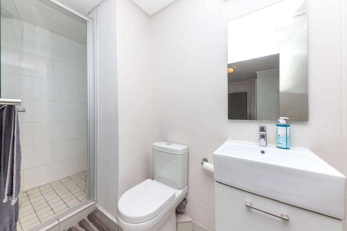 A clean and functional bathroom featuring a glass-enclosed shower, modern vanity basin with storage, and a wall-mounted mirror.