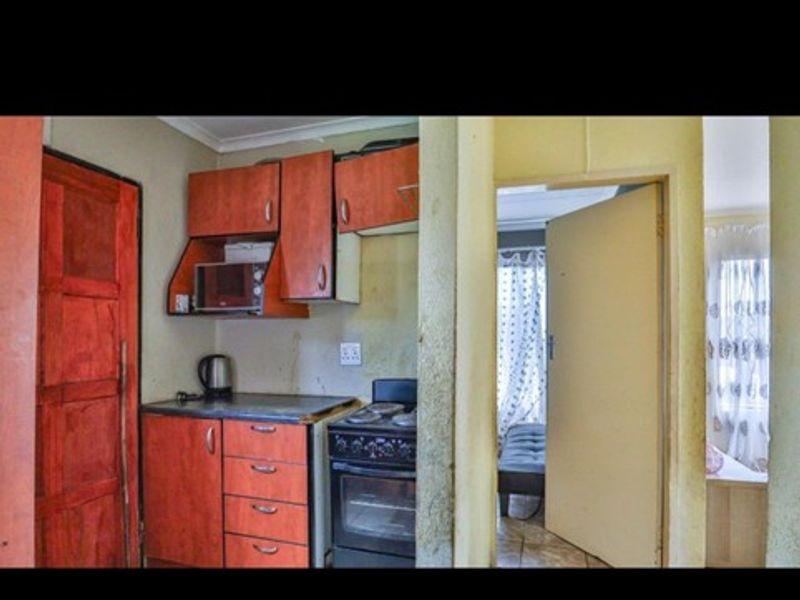 A compact kitchen area featuring dated wooden cabinetry, a freestanding stove, and direct access to an adjacent room.