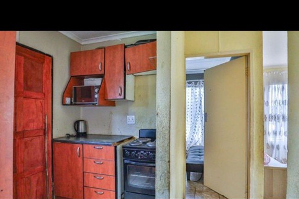 A compact kitchen area featuring dated wooden cabinetry, a freestanding stove, and direct access to an adjacent room.