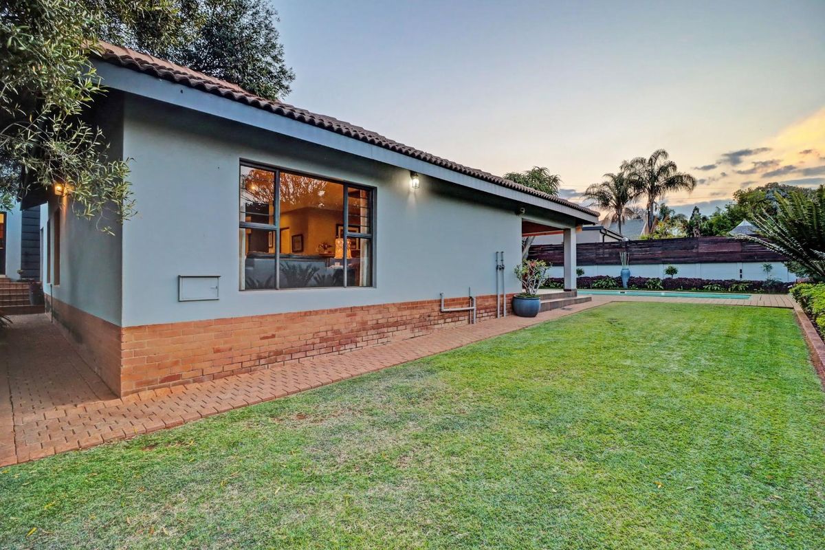 Rear view of the property featuring a well-maintained lawn, paved walkway, swimming pool, and a clean exterior facade with brick detailing.