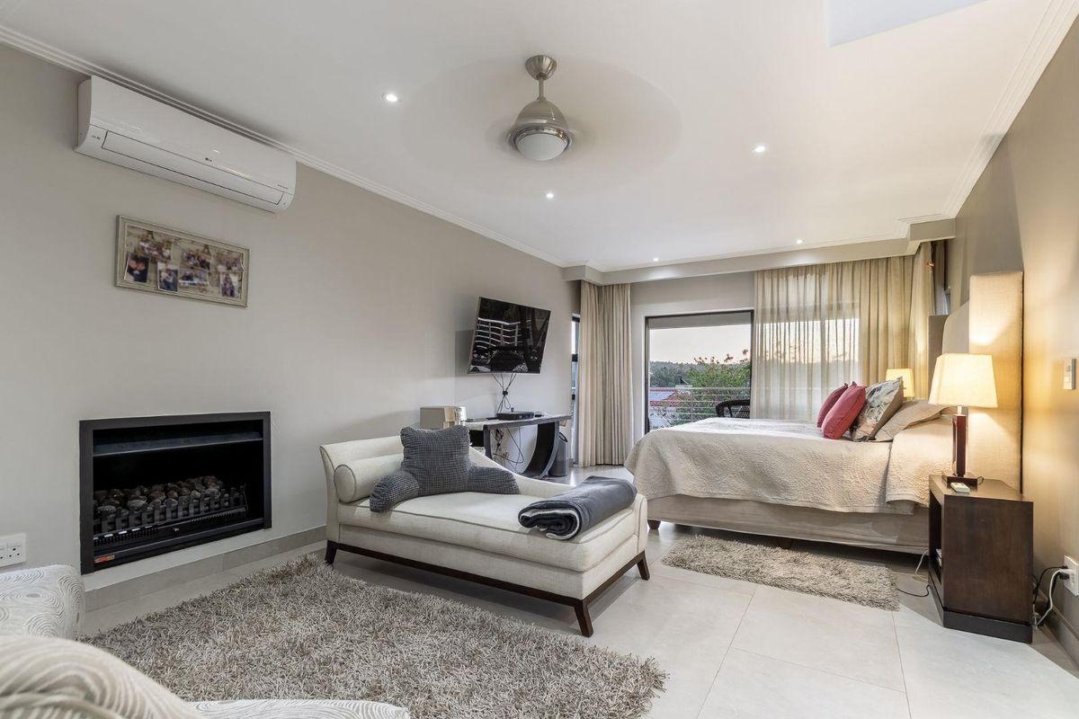 Spacious bedroom featuring a built-in fireplace, wall-mounted air conditioning unit, ceiling fan, and sliding glass doors leading to a private balcony.