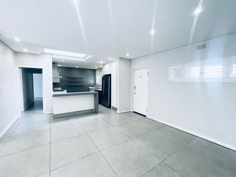 Modern open-plan living area featuring large format floor tiles, recessed lighting, and a sleek kitchen with a central island and built-in cabinetry.
