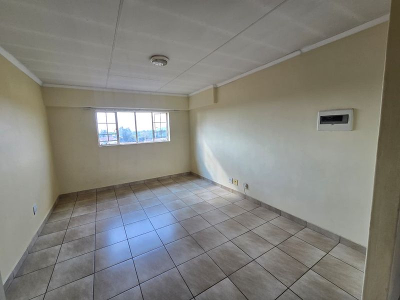 An empty, tiled living area featuring a window, ceiling light, and wall-mounted electrical distribution board, ready for personalization.