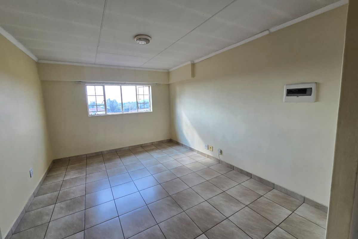 An empty, tiled living area featuring a window, ceiling light, and wall-mounted electrical distribution board, ready for personalization.