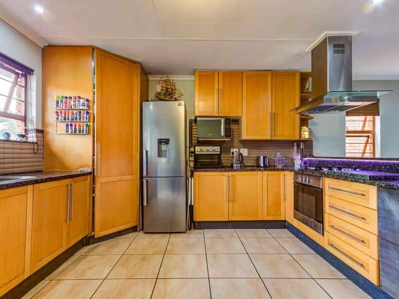 A functional kitchen featuring warm wood cabinetry, granite countertops, a stainless steel extractor fan, and a built-in oven with a gas hob.