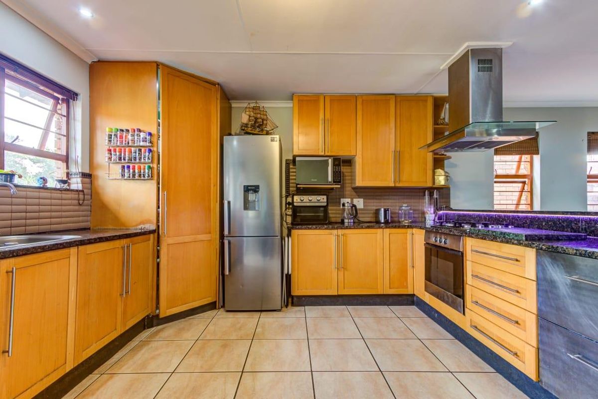 A functional kitchen featuring warm wood cabinetry, granite countertops, a stainless steel extractor fan, and a built-in oven with a gas hob.