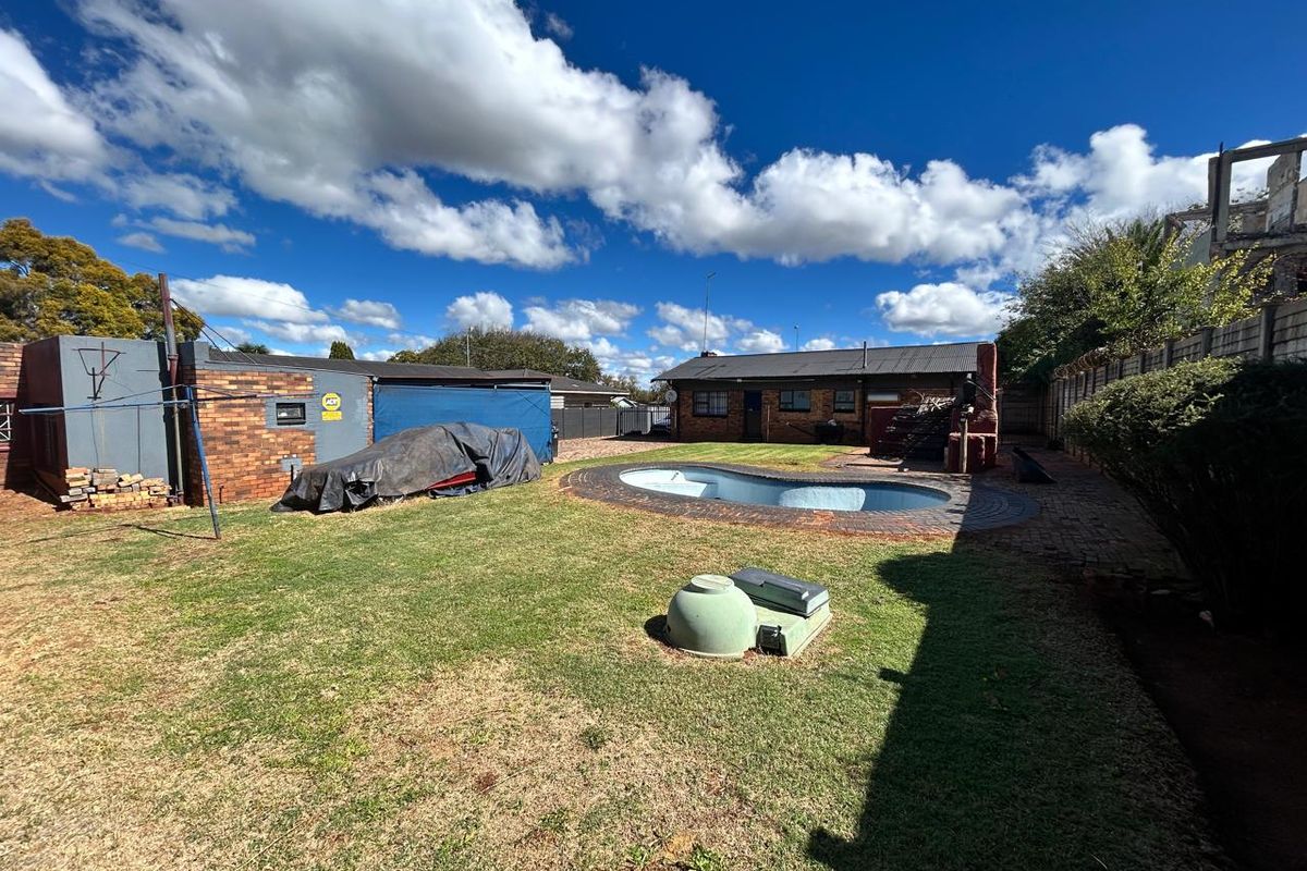 Rear garden featuring a swimming pool, brick paving, and a brick outbuilding structure under a clear blue sky.