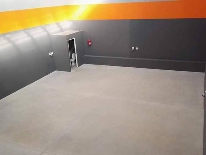 Spacious industrial utility area featuring smooth concrete flooring, painted walls with high-visibility accents, and a private enclosed toilet facility.