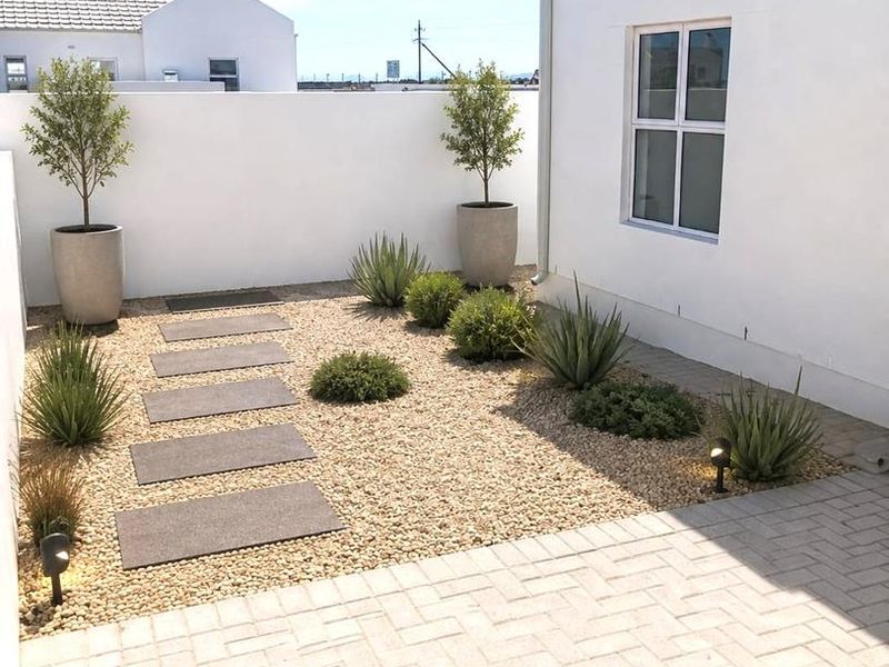 A well-maintained rear courtyard featuring a paved patio area, gravel landscaping with stone stepping stones, and clean white boundary walls.