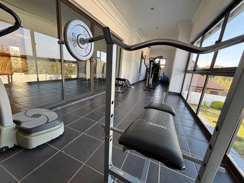 A bright, enclosed gym space featuring tiled flooring, recessed downlights, and extensive aluminium sliding doors providing natural light and garden views.
