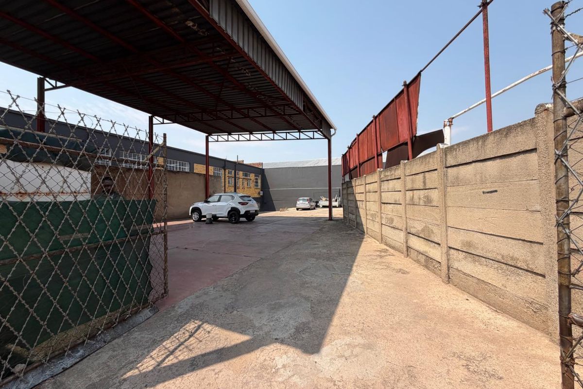 Rear exterior area featuring a large metal carport structure, concrete paving, and secure boundary walling with chain link and razor wire fencing.