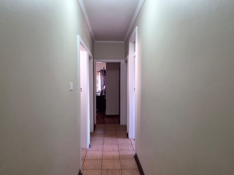 A clean, neutral hallway featuring tiled flooring and coved ceiling details, providing access to multiple rooms within the home.