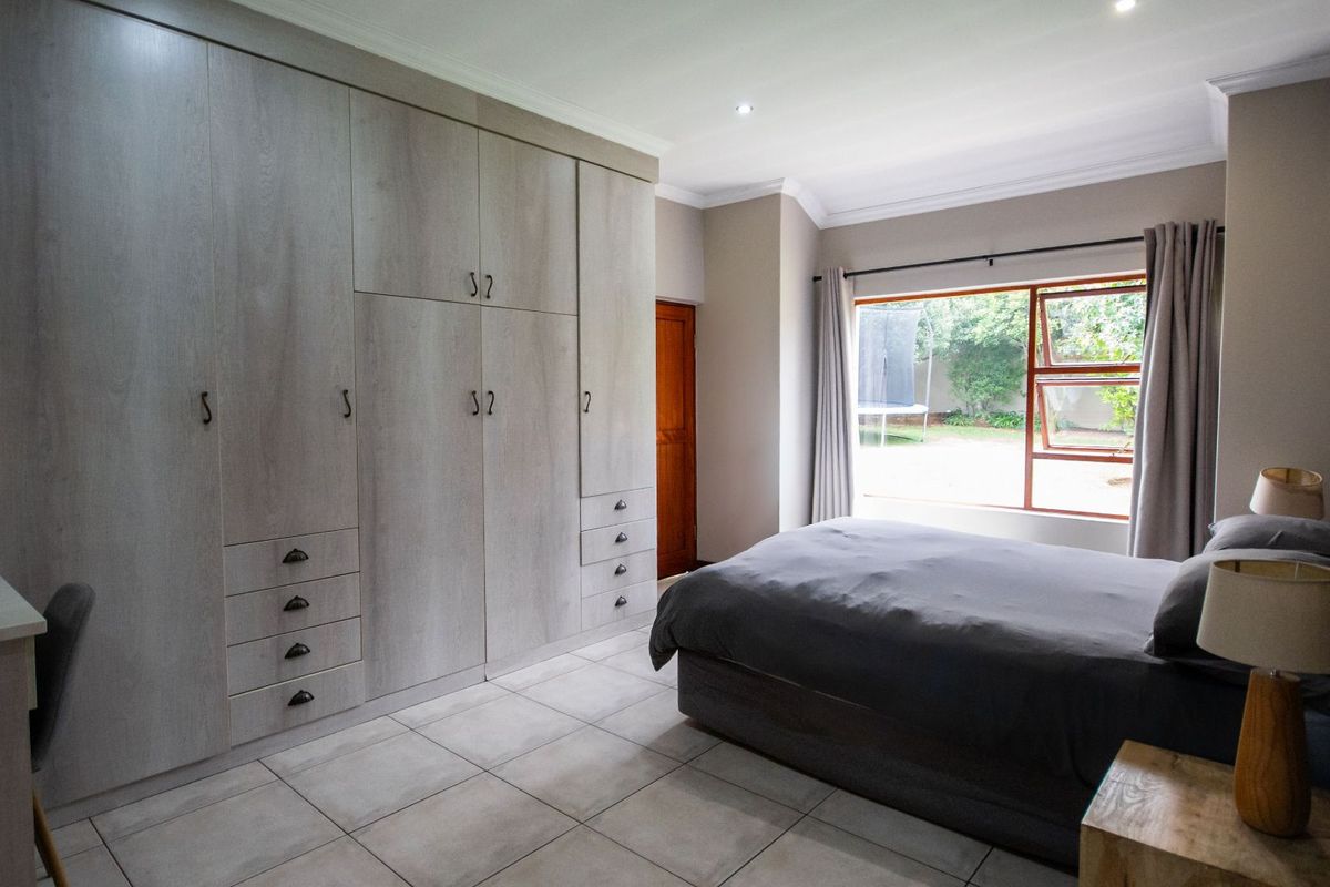 A well-lit bedroom featuring extensive built-in cabinetry with integrated drawers and shelving, tiled flooring, and a large window overlooking the garden.