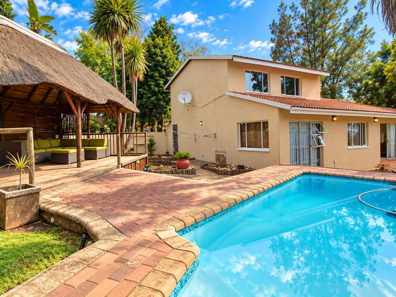 A well-maintained outdoor entertainment area featuring a swimming pool, brick-paved surround, and a spacious thatched lapa with timber decking.