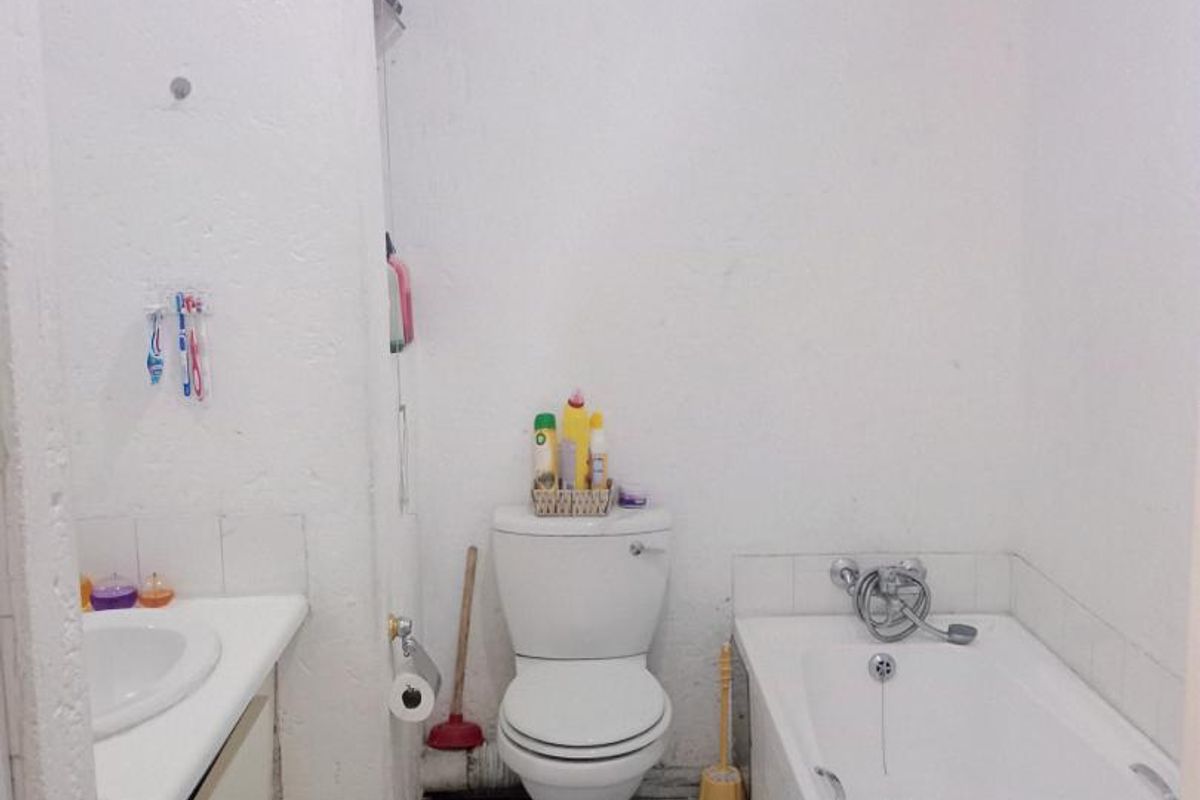 A compact bathroom featuring a built-in vanity, standard toilet, and a bathtub with chrome fixtures, requiring cosmetic updates to improve its overall condition.