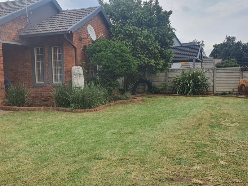A well-maintained rear garden featuring a brick-faced house, tiled roof, and secure precast concrete boundary walling.