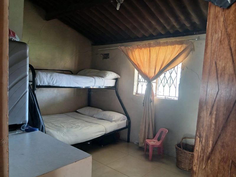 A bedroom featuring tiled flooring, security bars on the window, and an exposed beam ceiling, currently showing signs of wall plaster cracking.