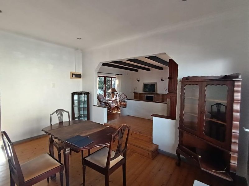 Open plan living and dining area featuring exposed timber ceiling beams, polished timber flooring, and a raised floor transition between spaces.
