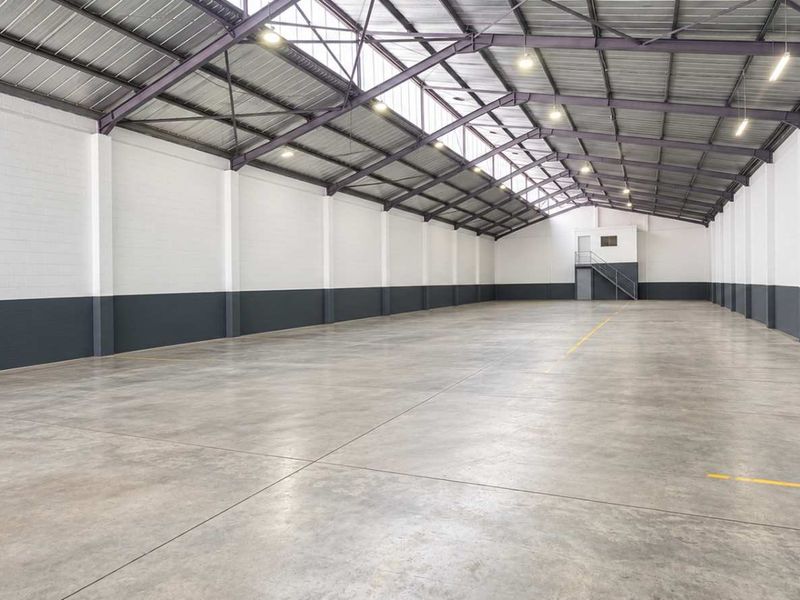 Spacious industrial warehouse unit featuring high ceilings with exposed steel trusses, durable concrete flooring, and clean painted blockwork walls.