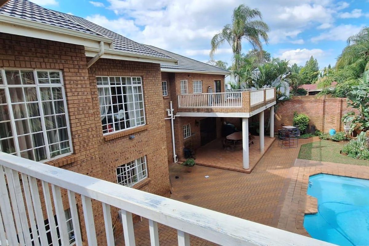 Rear view of a double-story brick house featuring a swimming pool, paved patio area, and an elevated balcony overlooking the garden.