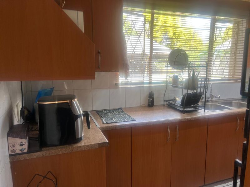 A functional kitchen featuring wood-look laminate cabinetry, tiled splashbacks, and a double bowl stainless steel sink with a window view.