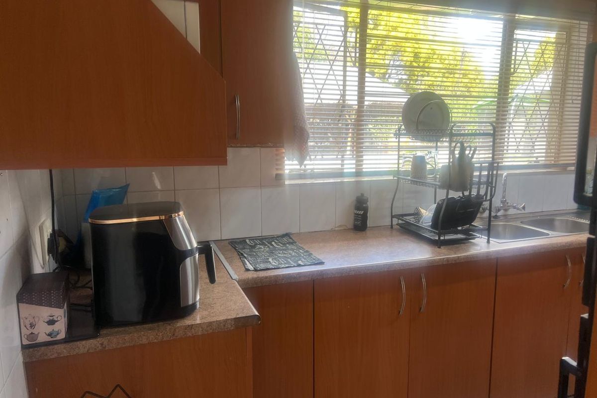 A functional kitchen featuring wood-look laminate cabinetry, tiled splashbacks, and a double bowl stainless steel sink with a window view.