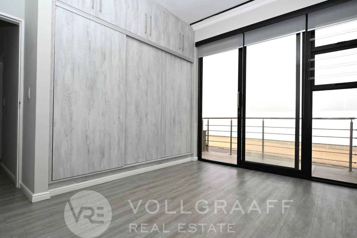 A bright bedroom featuring modern wood-look laminate flooring, extensive built-in cabinetry, and large sliding glass doors opening onto a private balcony.