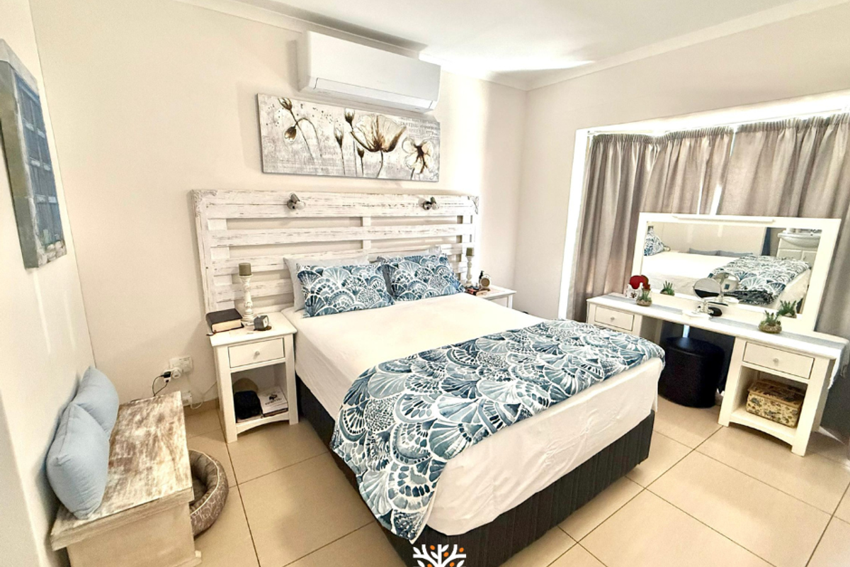 A well-maintained bedroom featuring tiled flooring, a wall-mounted air conditioning unit, and a large bay window with curtains.